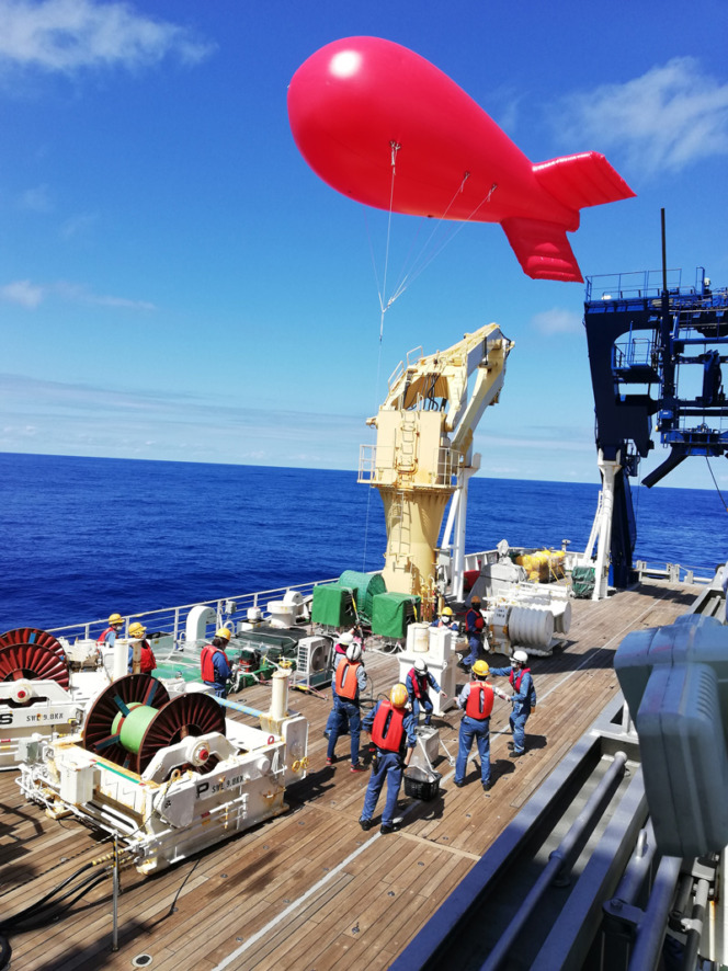 写真。船の作業甲板から係留気球を飛ばしている様子。