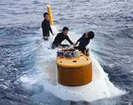 3月25日の伊豆・小笠原海溝海域はうねりが大きくスイマーも波を被りながら最後のガイド索を取り外します。（スイマーは通常2名ですが、新人の訓練のため3名で作業を行っています。）